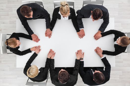 Business people holding hands sitting around empty table, unity and cooperation concept
