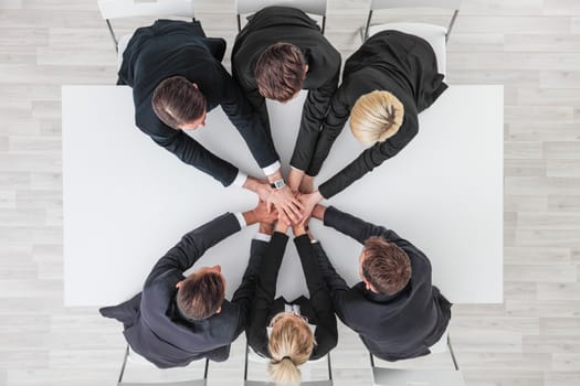 Business people team stacking hands sitting around white conference table in office