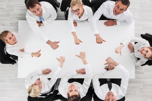 Business people showing thumbs up sitting around white conference table in office