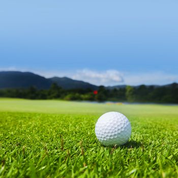 Golf ball on course, beautiful landscape with mountains on background