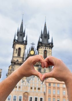 Close up man hands showing heart shape love symbol over cityscape with Cathedral of Our Lady before Tyn, Prague, Czech Republic