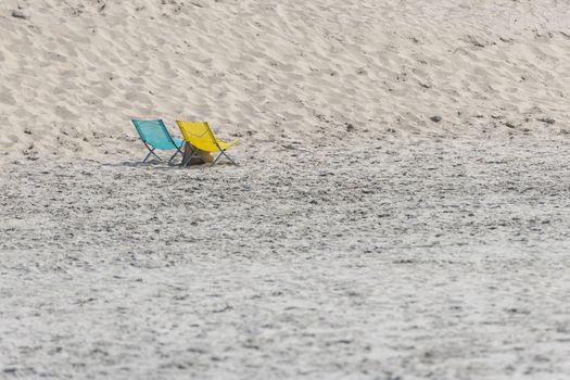 A blue and yellow folding chair on the North Sea Beach of Ameland in the North of Netherlands
