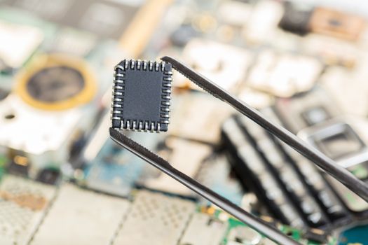 electronic chip in tweezers on background of the disassembled mobile phone