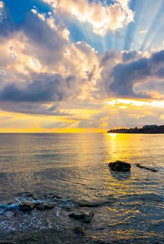 gorgeous sunrise at the seaside. sunbeams come from behind the cloud. sun reflects on rippled water surface. calm wave touch rocky shore. beautiful summer scenery and vacation concept