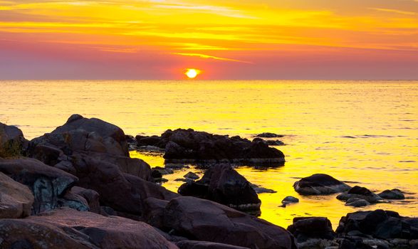 reddish sunrise over the sea with rocky shore. beautiful summer scenery and vacation concept