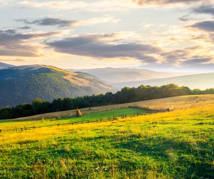 beautiful rural scenery in mountains at sunrise. haystack on the field behind the fence. outdated agriculture approach concept