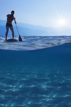 Stand up paddle boarding. Young man floating on a SUP board. Underwater view of sea, copy space for text