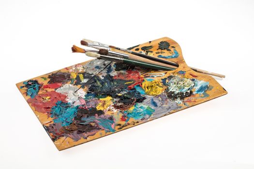 Old wooden palette with paints and brushes on an isolated studio background