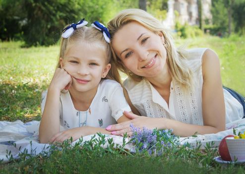 Mother and daughter lying on green grass in summer