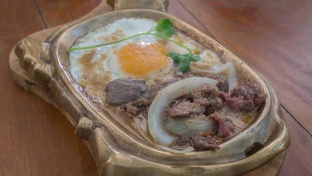 stir-fried beef with onion served with fried egg in hot pan , asian breakfast