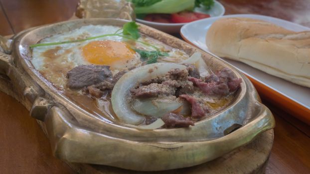 stir-fried beef with onion served with fried egg in hot pan , asian breakfast