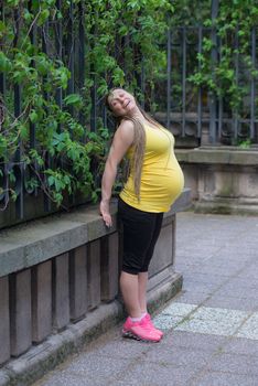 Smiling pregnant woman with yellow vest is exercising outdoors.