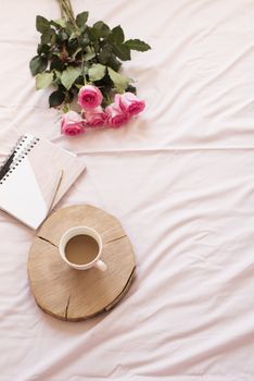 Coffee, pink roses, noteboo.ks in bed on pink sheets. Freelance fashion home femininity workspace in flat lay style