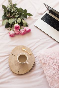 Roses, laptop, notebooks and smartphone in bed on pink sheets. Freelance fashion home femininity workspace in flat lay style.