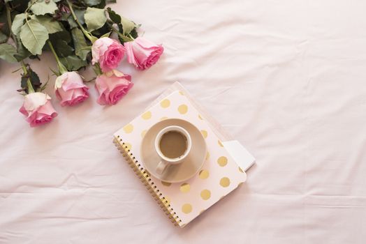 Coffee in bed on pink sheets. Roses, notebooks around. Freelance fashion home femininity workspace