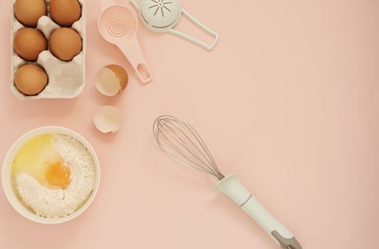 Ingredients and kitchen bake tools for cooking cake or sweets - eggs, flour, whisk on a pastel punchy pink background. Top view of a holiday baking still life