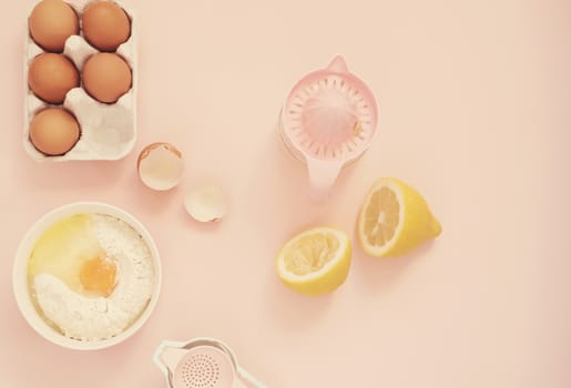 Ingredients and kitchen bake tools for cooking lemon cake or sweets - eggs, flour, hand juicer on a pastel punchy pink background. Top view of a holiday baking still life