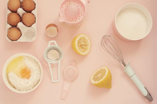 Ingredients and kitchen bake tools for cooking lemon cake or sweets - eggs, flour, hand juicer, sugar on a pastel punchy pink background. Top view of a holiday baking still life