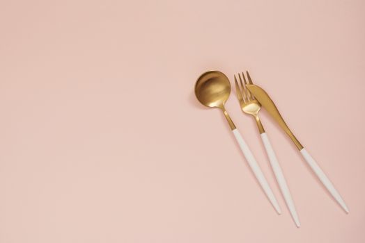 Gold cutlery. Golden spoon set, golden knife, spoon and fork on the table. Luxury spoon set top of view. Pastel punchy pink background