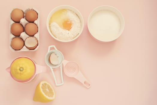 Ingredients and kitchen bake tools for cooking lemon cake or sweets - eggs, flour, sugar, hand juicer on a pastel punchy pink background. Top view of a holiday baking still life