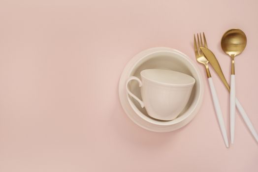 Gold cutlery. Golden spoon set, golden knife, spoon, fork, coffee cup and empty dishes on the table. Luxury spoon set top of view. Pastel punchy pink background