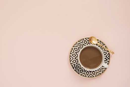 Coffee on a pastel punchy pink background.  Latte in a white, black and gold coffee cup. Feminine workplace concept. Freelance fashion comfortable femininity workspace with coffee.
