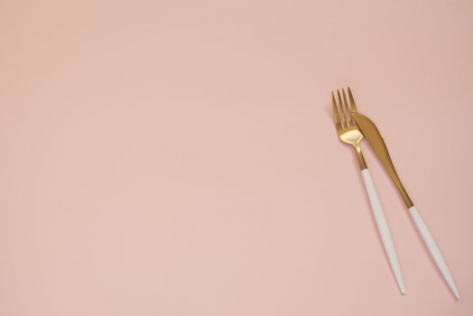 Gold cutlery. Golden spoon set, golden knife and fork on the table. Luxury spoon set top of view. Pastel punchy pink background 