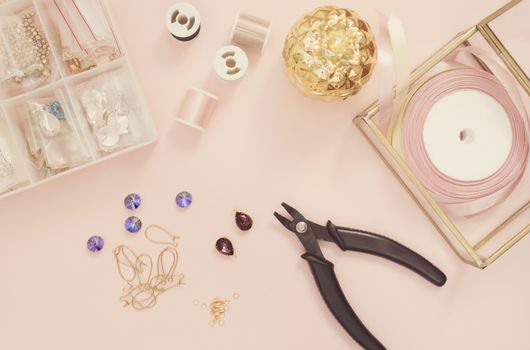 Jewelry designer workplace. Handmade, craft concept. Materials for making jewelry ? pliers, crystals? ear wires, ribbons. Freelance workspace in flat lay style. Pastel pink and gold.