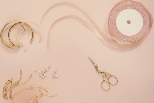 Jewelry designer workplace. Handmade, craft concept. Materials for making jewelry ? golden scissors, ribbons, gold tubes, bracelet settings. Freelance workspace in flat lay style. Pastel pink and gold