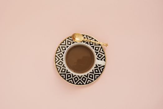 Coffee on a pastel punchy pink background.  Latte in a white, black and gold coffee cup. Feminine workplace concept. Freelance fashion comfortable femininity workspace with coffee