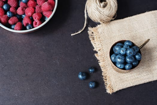 Fresh raspberries and blueberries dark picture with copy space on left. Fresh fruits, berries in an old copper cup, bowl. Dark Styled Stock Photo, Black Background