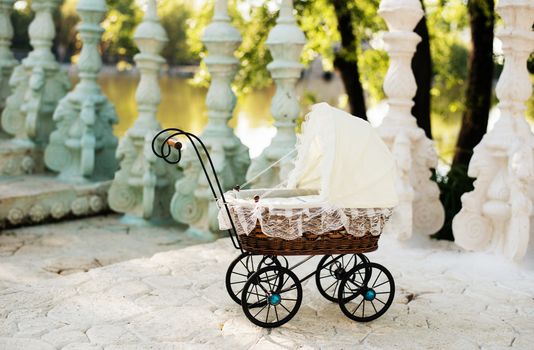 Doll's pram. Vintage doll stroller placed on the stairs to a beautiful lake. Retro cart dolls made of rattan and white lace.