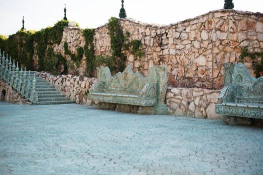 Stone walkway. Alley in beautiful garden with stone benches, flight of stairs, flowers and trees around. Summer in the garden