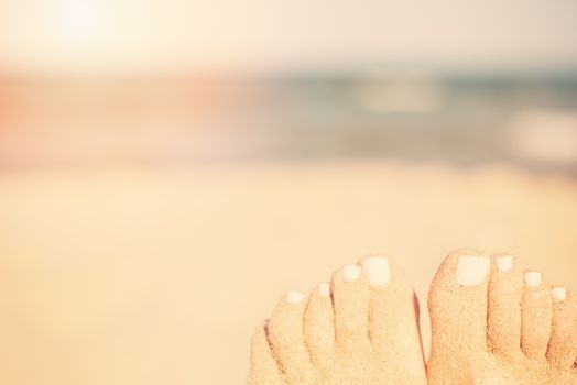 Holiday concept. Woman feet close-up relaxing on beach, enjoying sun and splendid view. Sandy feet on the beach. Sun, sun haze, glare