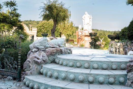 Old baroque stairs, outdoors. Stairs made of stone. Alley in beautiful garden with flowers and trees and frogs around.