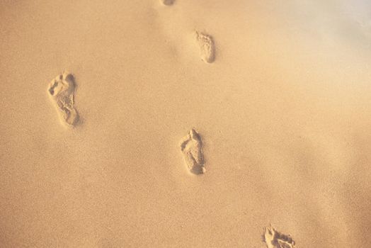 Footprints in the sand. Human footprints leading away from the viewer. A row of footprints in the sand on a beach in the summertime. Sun, sun haze, glare. Copy space