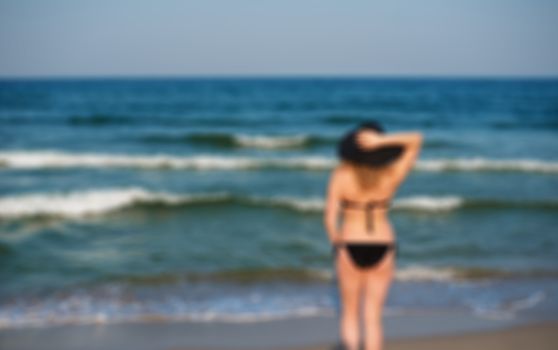 Blurred picture of  young lady in black hat on the beach. Pretty girl looking at distance on blurred lens flare beach, sea background. Sun, glare. Copy space 