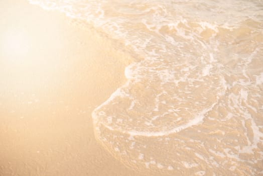 Sand and wave background. Soft wave of the turquoise sea on the sandy beach. Natural summer beach background with copy space. Sun, sun haze, glare