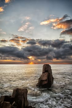 Sunrise over a rocky beach. Colorful clouds reflecting in the sea. Dramatic sunrise over the Black Sea, Bulgaria