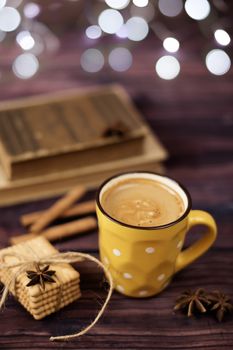 Mug of coffee, cookies, star anise, cinnamon, old books. Blurred lights, wooden background. Winter time, Rustic background with beautiful Christmas lights of bokeh.