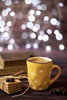 Mug of coffee, cookies, star anise, cinnamon, old books. Blurred lights, wooden background. Winter time, Rustic background with beautiful Christmas lights of bokeh.