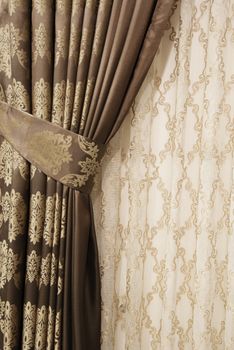 Part of beautifully draped curtain on the window in the room. Close up of piled curtain. Luxury curtain, home decor. Gold and brown panels. Lace drapery