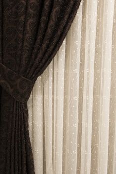 Beautifully draped long curtain on the window in the room. Close up of piled curtain. Luxury curtain, home decor. Brown panels. White lace drapery