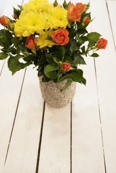 Vase of flowers on a white rustic table. Top view. Rustic vase with orange roses and yellow chrysanthemums. White background, empty place, copy space