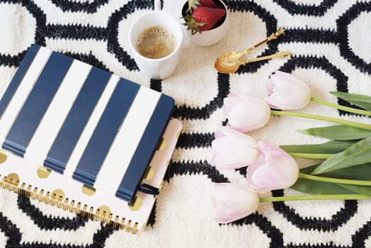 Coffee, strawberries, notebooks on Scandinavian rug. Pink Tulips and Gold Spoons. White black pattern and gold theme. Lifestyle concept