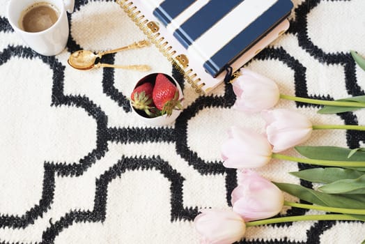 Coffee, strawberries, notebooks on Scandinavian rug. Pink Tulips and Gold Spoons. White black pattern and gold theme. Lifestyle concept. Copy Space