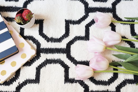 Coffee, strawberries, notebooks on Scandinavian rug. Pink Tulips and Gold Spoons. White black pattern and gold theme. Lifestyle concept. Copy Space