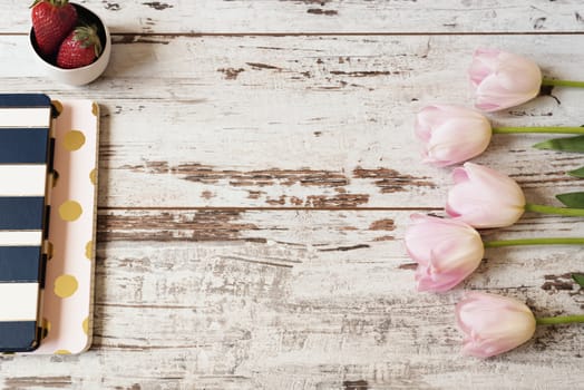 Stunning pink tulips, stripe notebooks and strawberries on white light rustic wooden background. Copy space, floral frame. Wedding, gift card, valentine's day or mothers day background