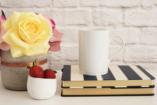 Coffee Cup Product Display. Coffee Mug On Striped Design Notebooks. Strawberries In Gold Bowl, Vase With Pink Roses