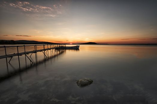 A traditional wooden fishing boat in the sea. Boat in the end of the old wooden pier. Fishing boat tied up in harbor at the end of the day. Sunset near the Black Sea coast